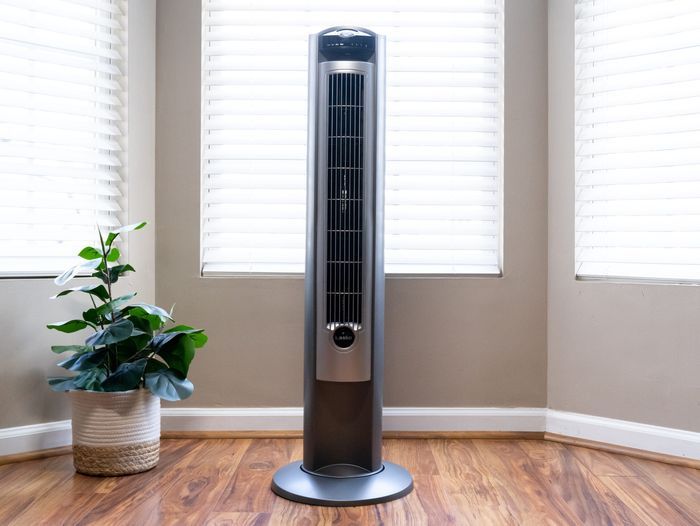 Lasko oscillating tower fan in front of a bay window, tan walls, and standing on a hardwood floor. Lead image for the best tower fan buying guide.