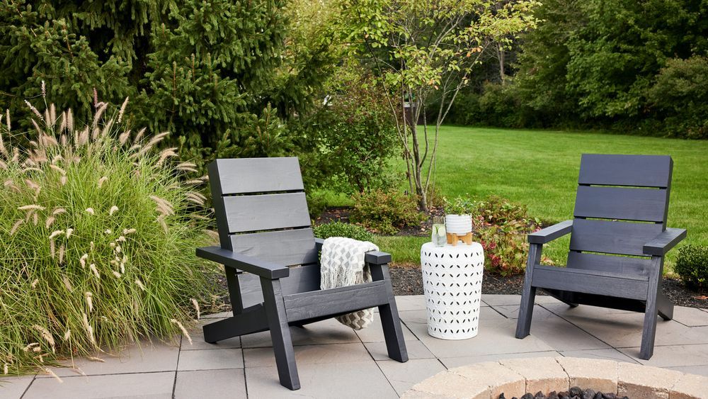 Two modern adirondack chairs painted black in a back yard.