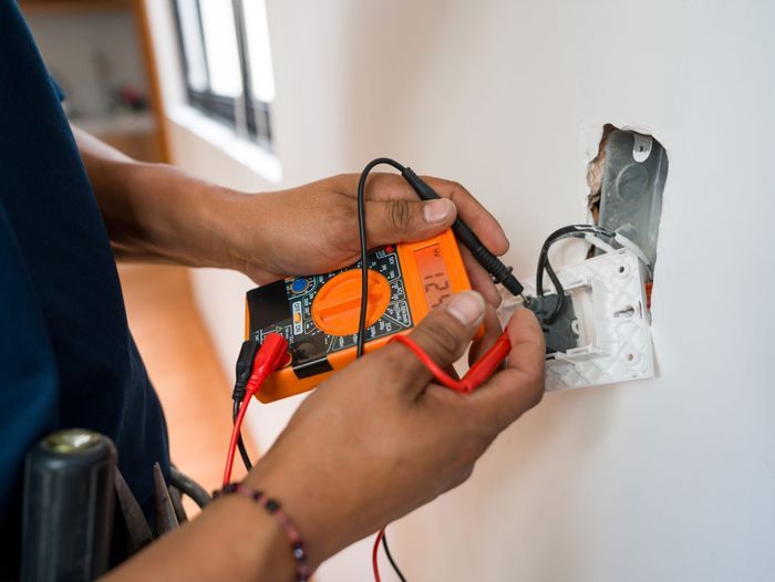 Close-up on an electrician fixing an electrical outlet and measuring the voltage at a house - home improvement concepts