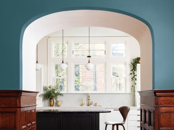 Arched hallway leading into a kitchen with a bold blue/green color