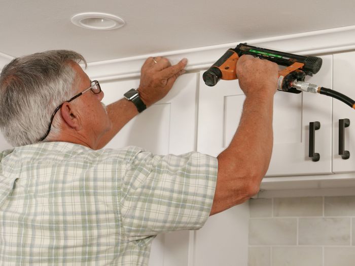 Tom Silva installing crown molding above a kitchen Cabinet.