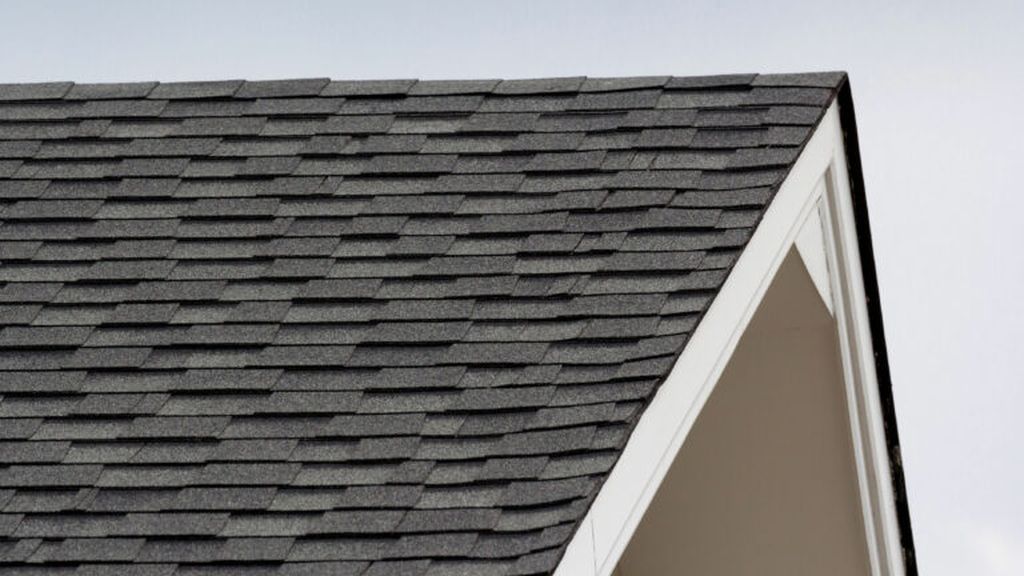 A triangular roof with black shingles on a white trusses