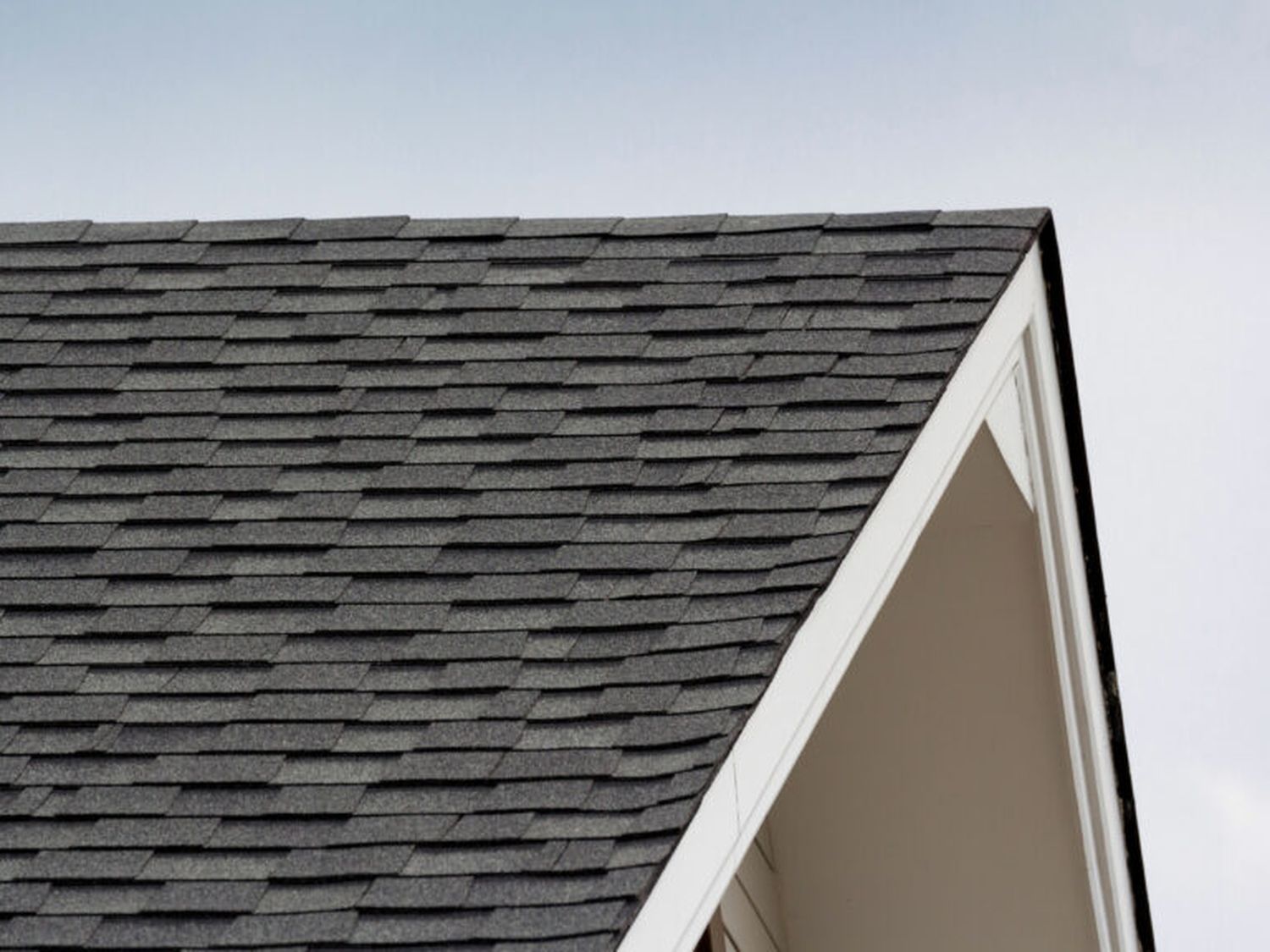 A triangular roof with black shingles on a white trusses